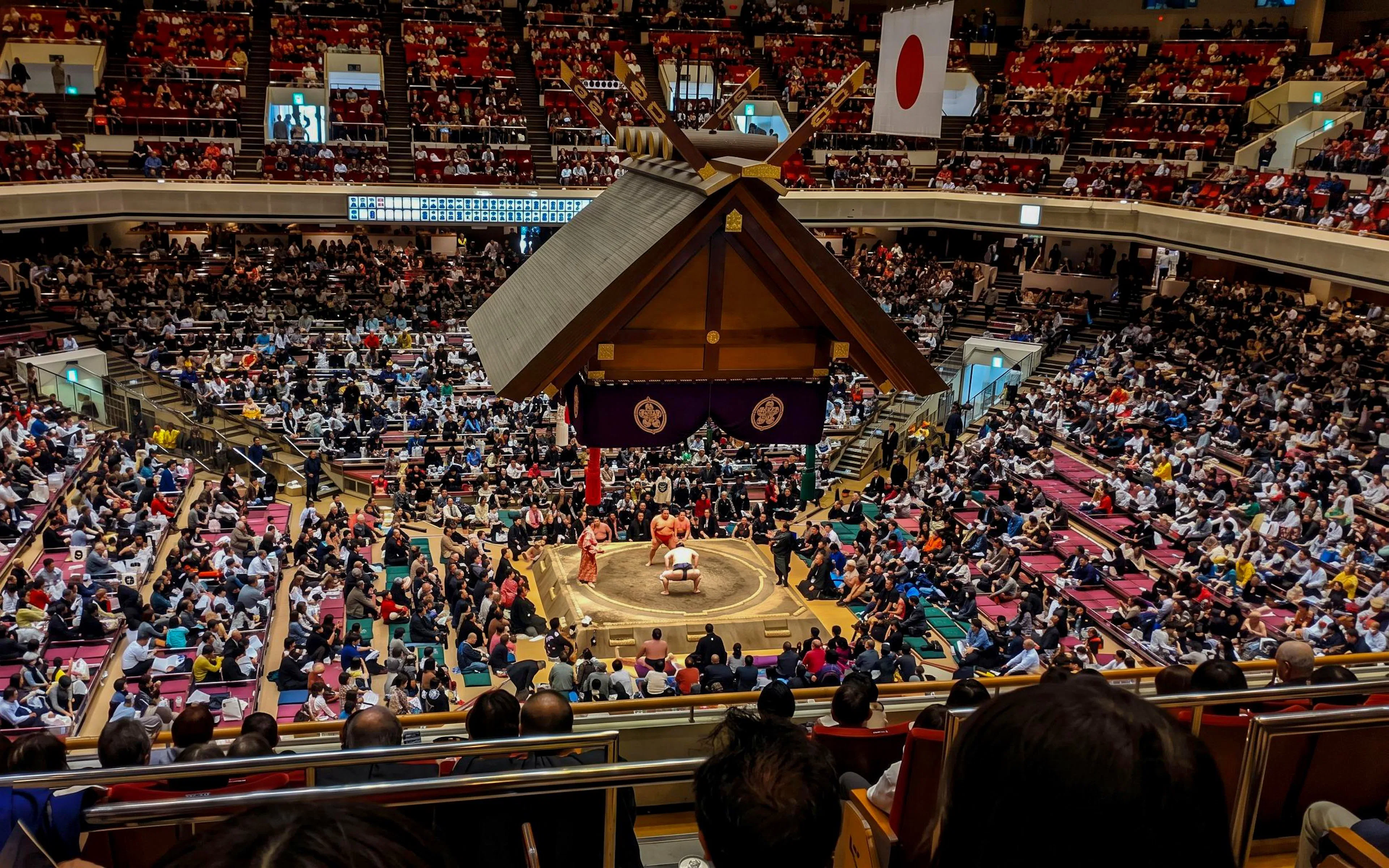 Crowded arena in Tokyo during a Grand Sumo Tournament with spectators watching a match.