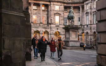 Tour group exploring historic Edinburgh courtyard with statue, part of Witches of Edinburgh tour.