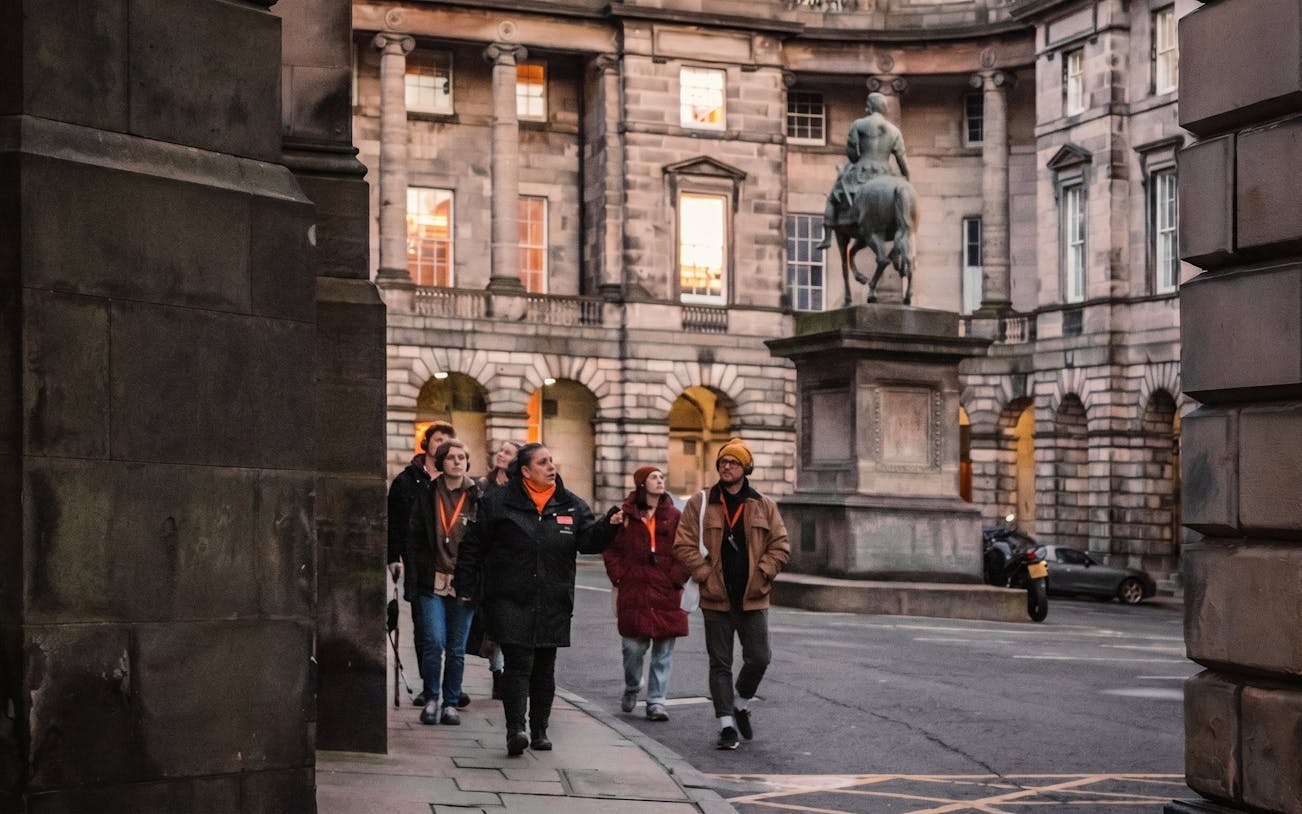 Tour group exploring historic Edinburgh courtyard with statue, part of Witches of Edinburgh tour.