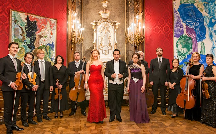 Vienna Baroque Orchestra musicians in formal attire with instruments in an ornate concert hall.