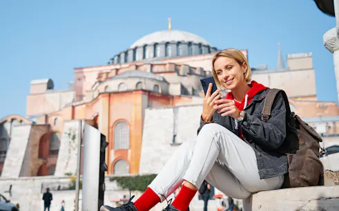 Traveler using smartphone with 4G E-Sim in front of Hagia Sophia, Istanbul.