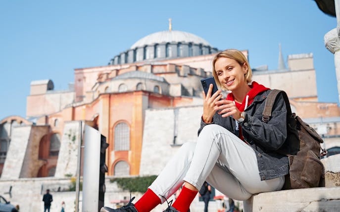 Traveler using smartphone with 4G E-Sim in front of Hagia Sophia, Istanbul.