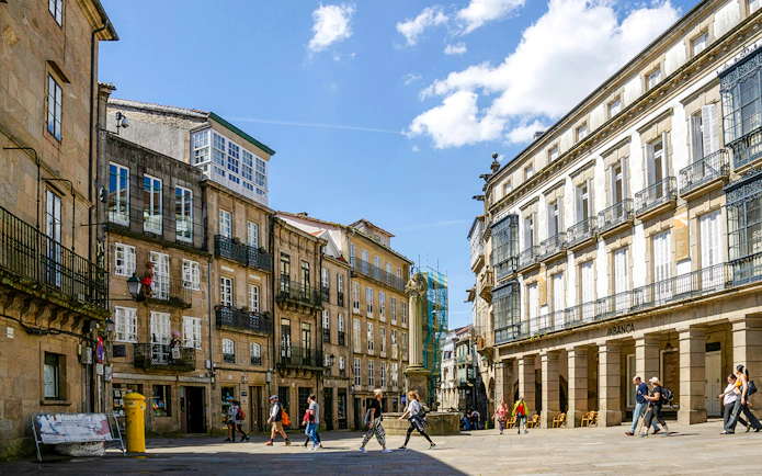 Praza De Cervantes in Santiago de Compostela with traditional buildings and people walking.