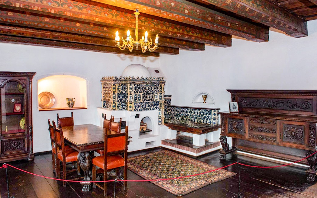 Dining room with ornate wood furniture and tiled stove inside Bran Castle, Romania.