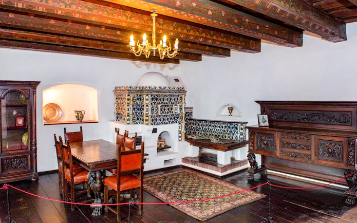Dining room with ornate wood furniture and tiled stove inside Bran Castle, Romania.