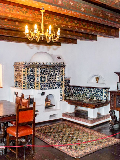 Dining room with ornate wood furniture and tiled stove inside Bran Castle, Romania.