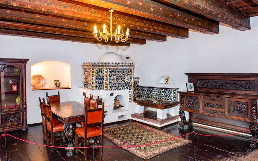 Dining room with ornate wood furniture and tiled stove inside Bran Castle, Romania.