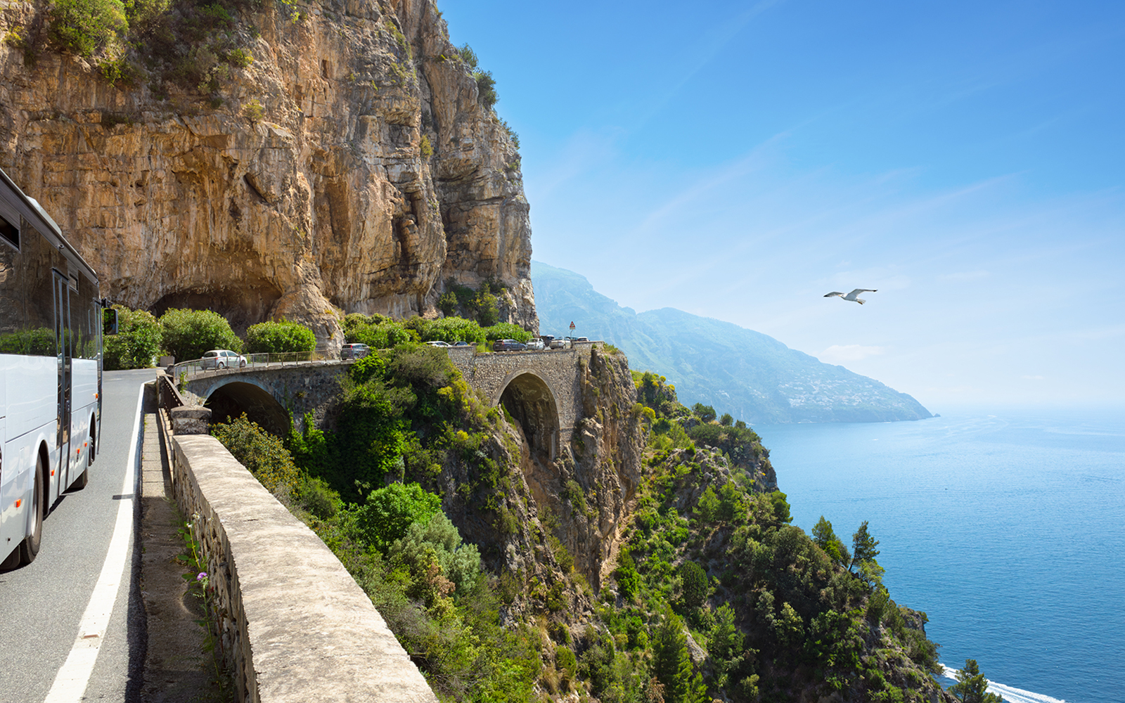 Coastal road on Amalfi Coast with bus and cars heading to Positano, Italy.