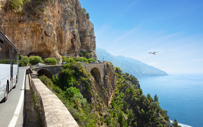 Coastal road on Amalfi Coast with bus and cars heading to Positano, Italy.