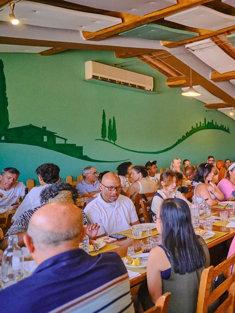 People dining at a long table during Pisa, Siena, and San Gimignano day trip.