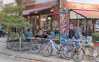 Outdoor cafe scene in St. Pauli with people dining and street art on walls.