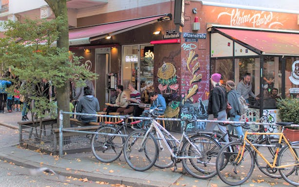 Outdoor cafe scene in St. Pauli with people dining and street art on walls.