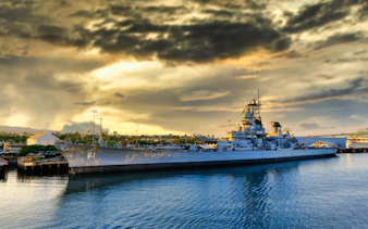 Battleship docked at harbor for guided and self-guided museum tours with scavenger hunt access.