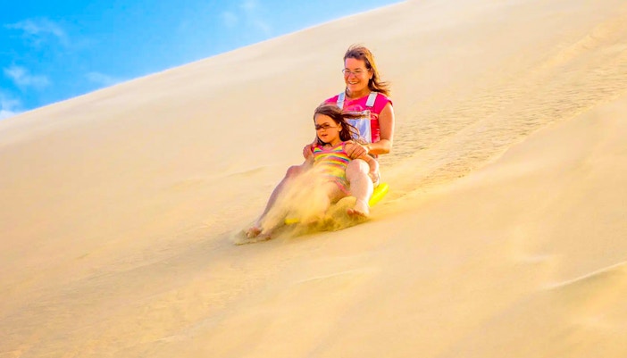 Family sandboarding at Dubai desert safari during sunset.