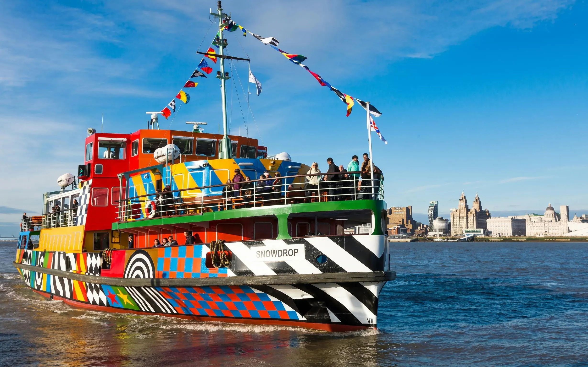 Colorful ferry on Mersey River with Liverpool skyline in background.