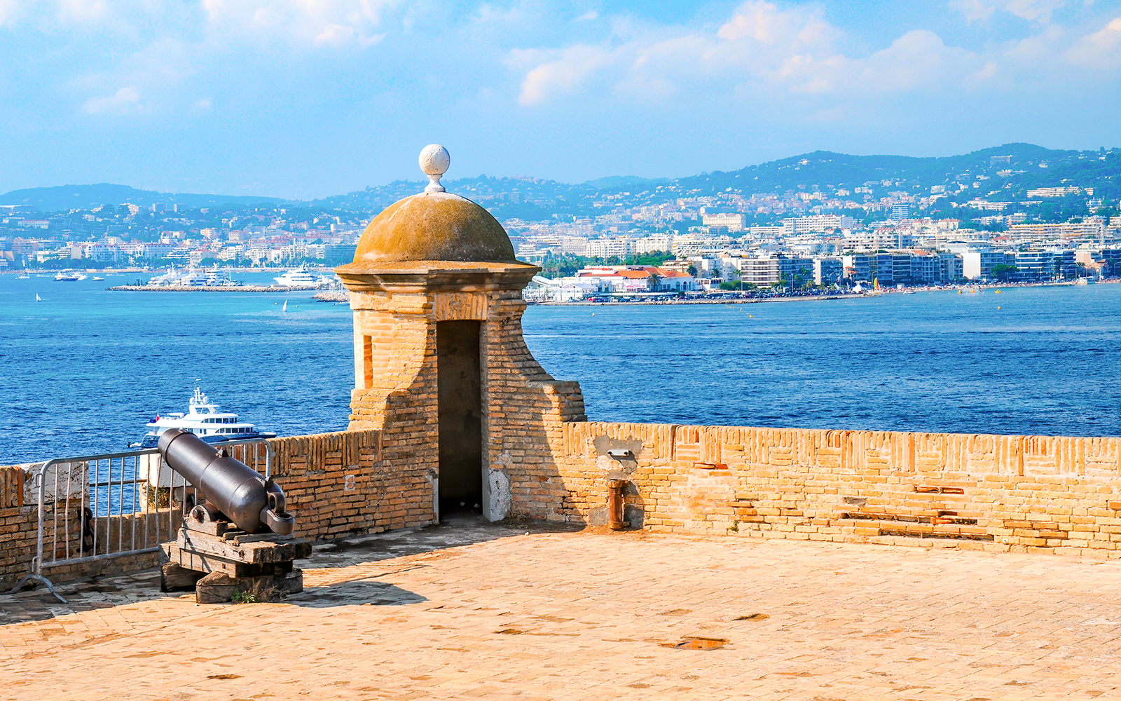 Fort wall with cannon overlooking Cannes harbor and cityscape, seen on a boat tour to Îles de Lérins.