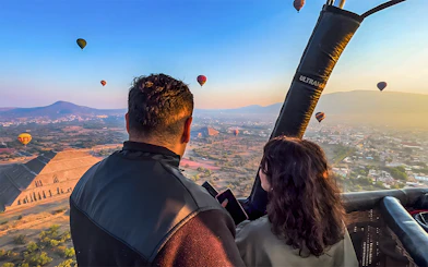 Passengers in hot air balloon over Teotihuacan pyramid, Mexico, with other balloons in the sky.