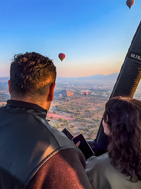 Passengers in hot air balloon over Teotihuacan pyramid, Mexico, with other balloons in the sky.