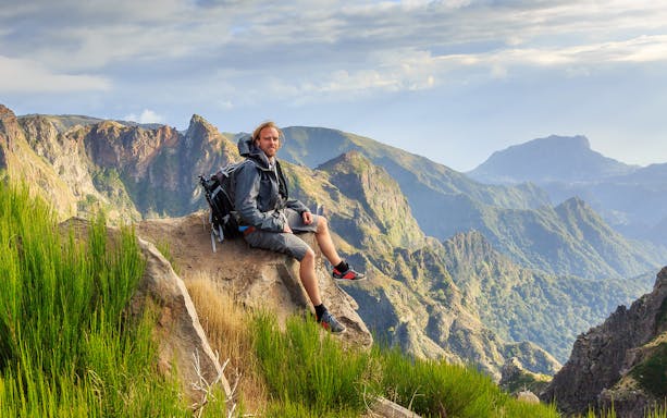 Hiker resting on a rock with a view of Areiro Peak and Nun's Valley in the background.