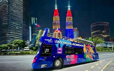Open-top bus in Kuala Lumpur with Petronas Towers illuminated at night.