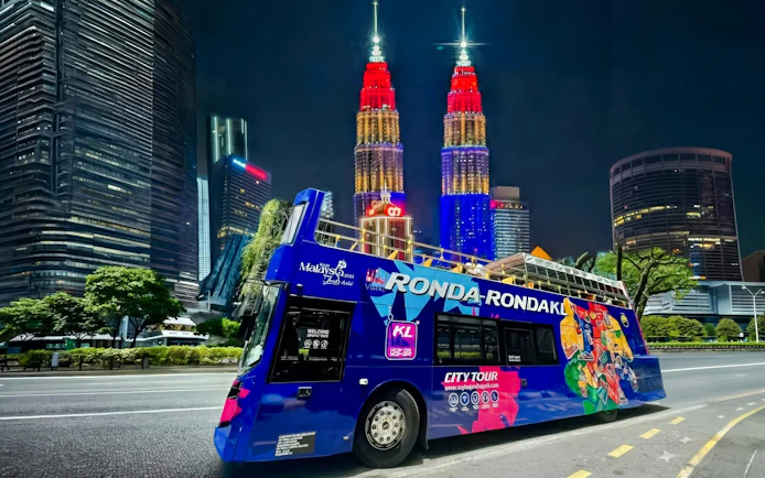 Open-top bus in Kuala Lumpur with Petronas Towers illuminated at night.