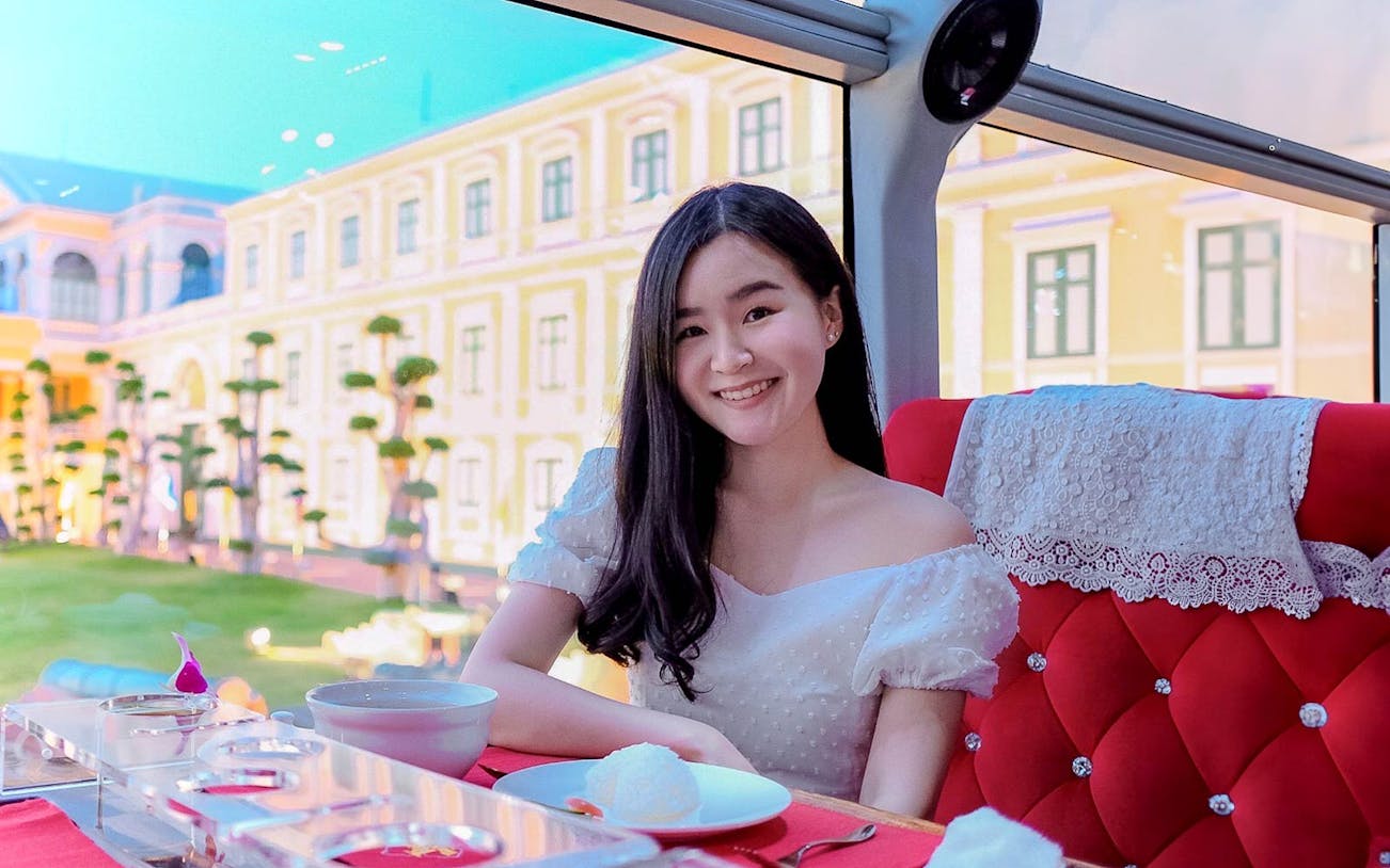 Woman enjoying meal on Thai bus food tour with historic building view.