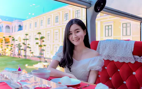 Woman enjoying meal on Thai bus food tour with historic building view.