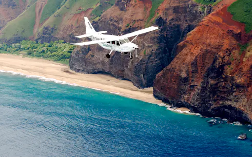 Small plane flying over Na Pali Coast, Kauai, showcasing cliffs and ocean during air tour.
