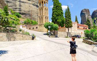 Tourist photographing Byzantine Church bell tower in Meteora, Greece.