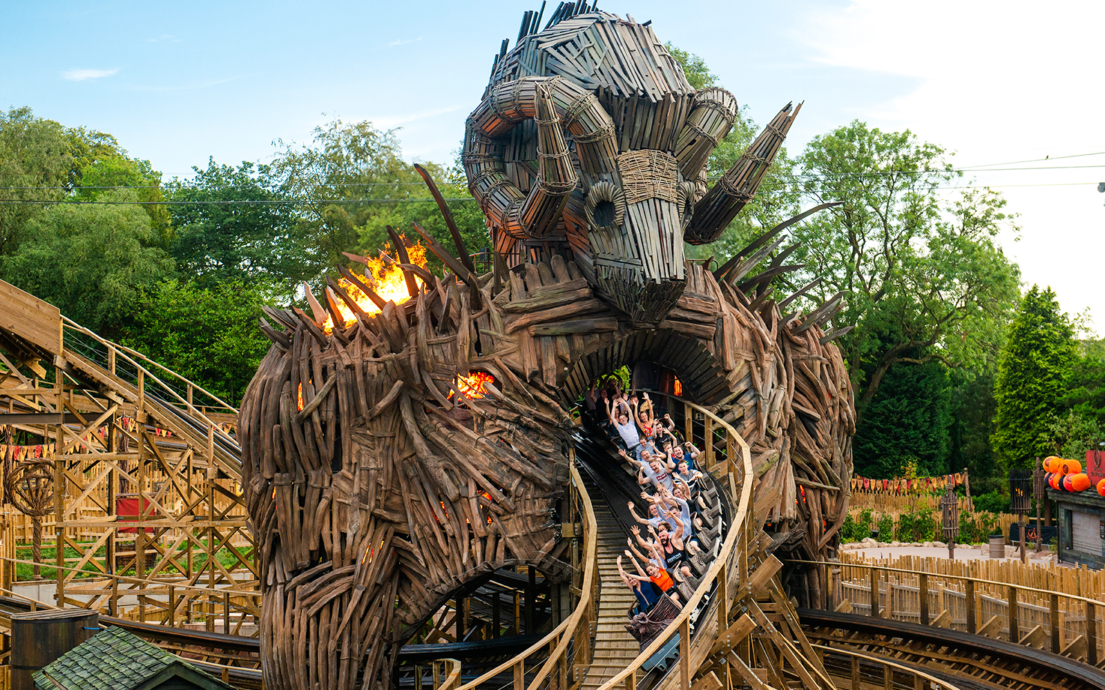 Riders on The Wicker Man roller coaster at Alton Towers, passing through a wooden structure with flames.