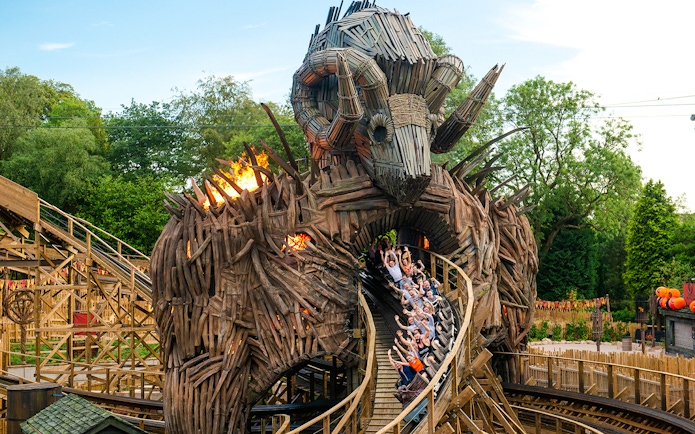 Riders on The Wicker Man roller coaster at Alton Towers, passing through a wooden structure with flames.
