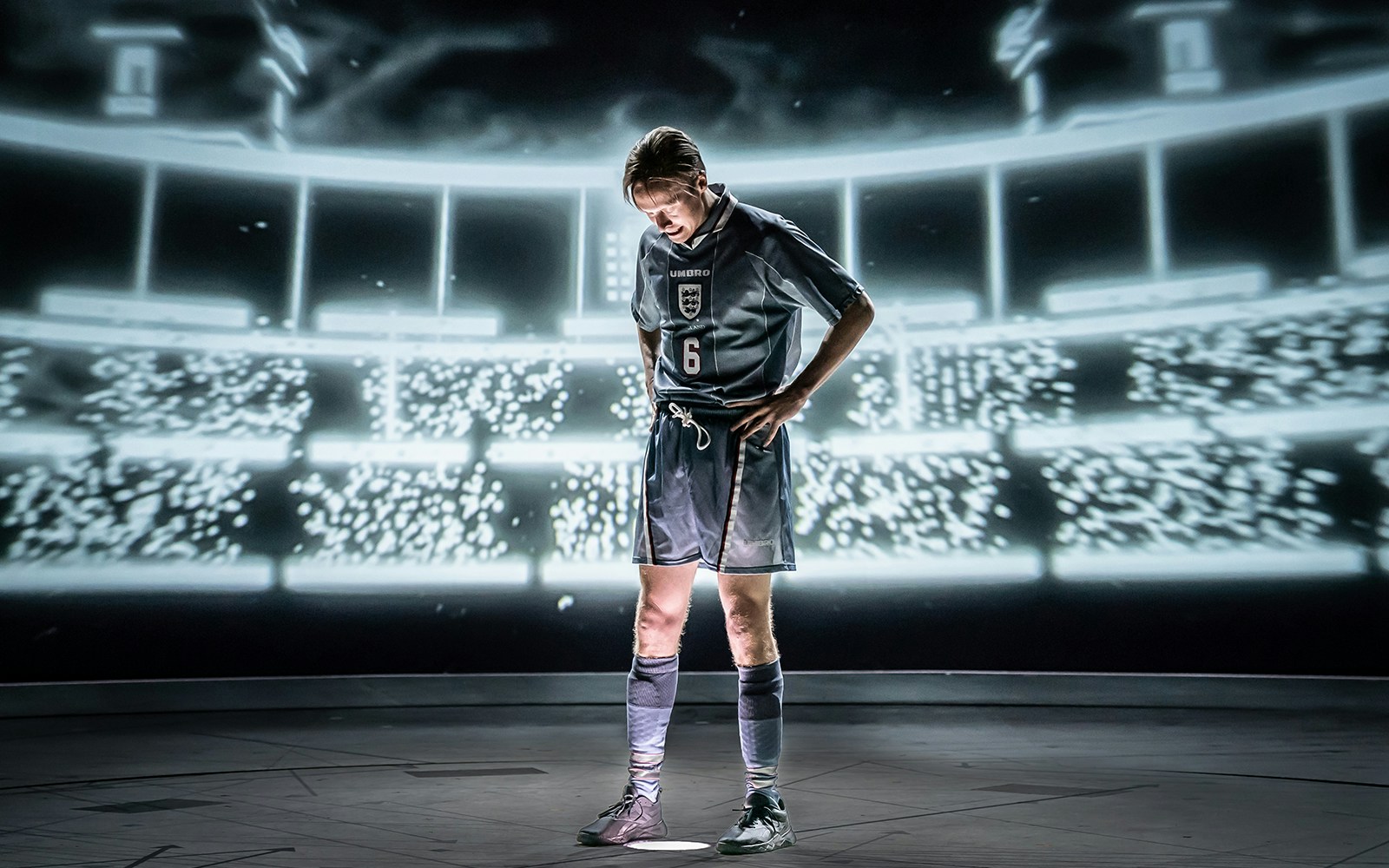 Football player in England jersey standing in a stadium with bright lights.