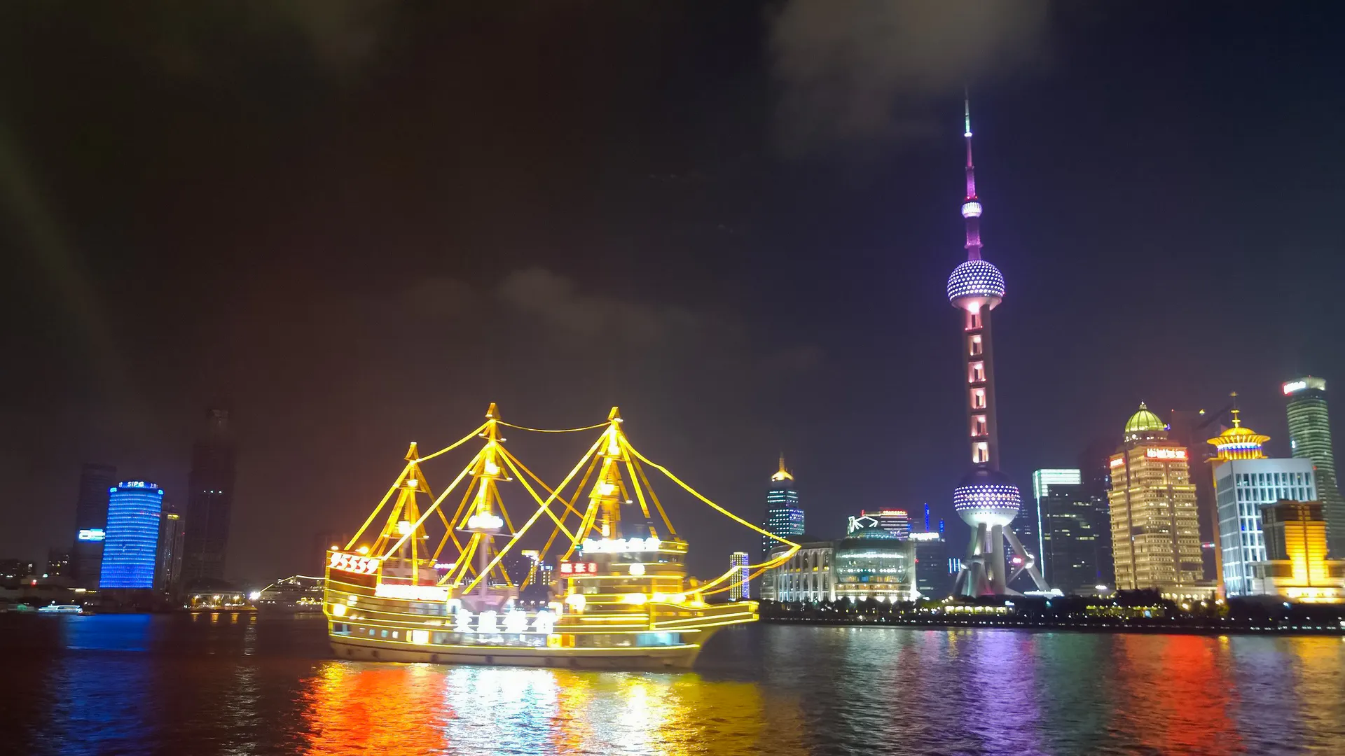 Shanghai Oriental Pearl Tower and illuminated boat at night.