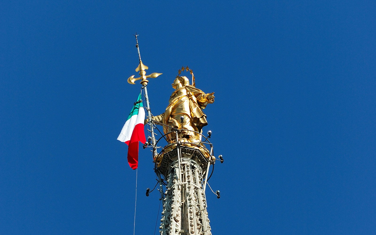 Statue of Madonnina with Italian flag atop Milan Cathedral spire.