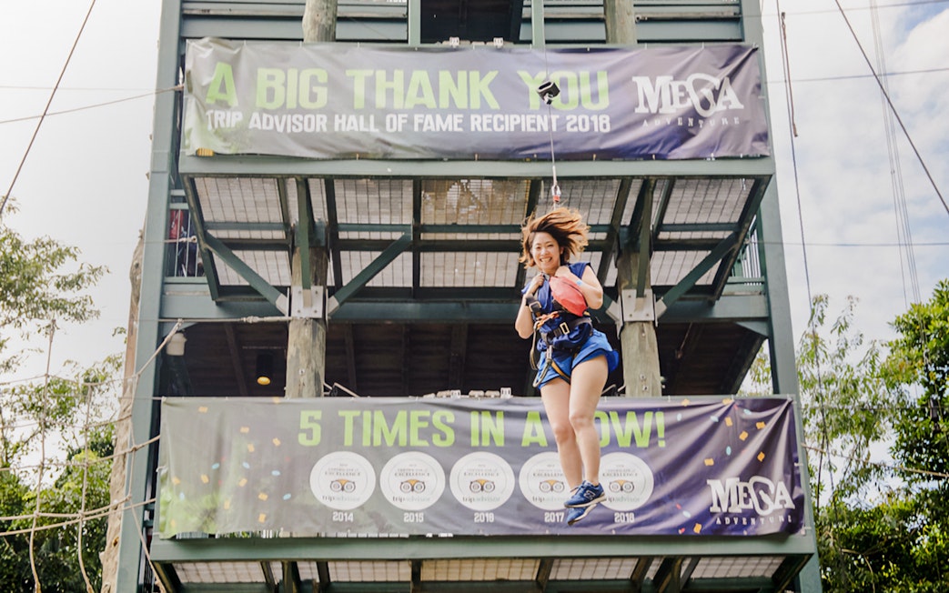 Person ziplining at Mega Adventure Park, Singapore, with award banners in the background.