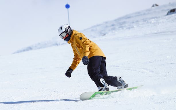 Snowboarder in yellow jacket on snowy slope with Ultimate Starter Skiing Pass.