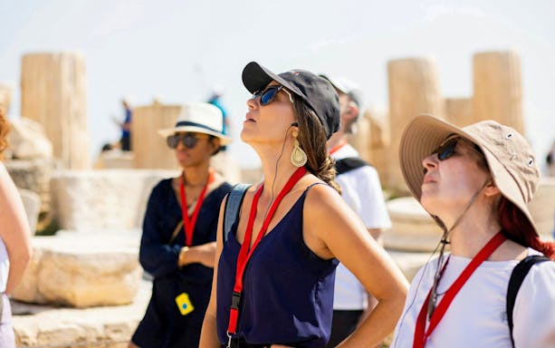 Tourists on a guided tour at the Acropolis in Athens, observing ancient ruins.