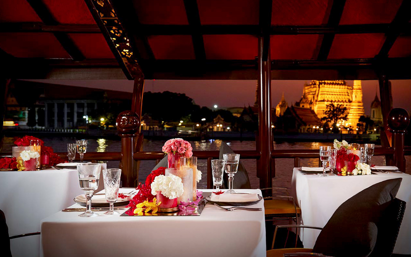 Elegant dining setup on Manohra Dinner Cruise with Wat Arun view in Bangkok.