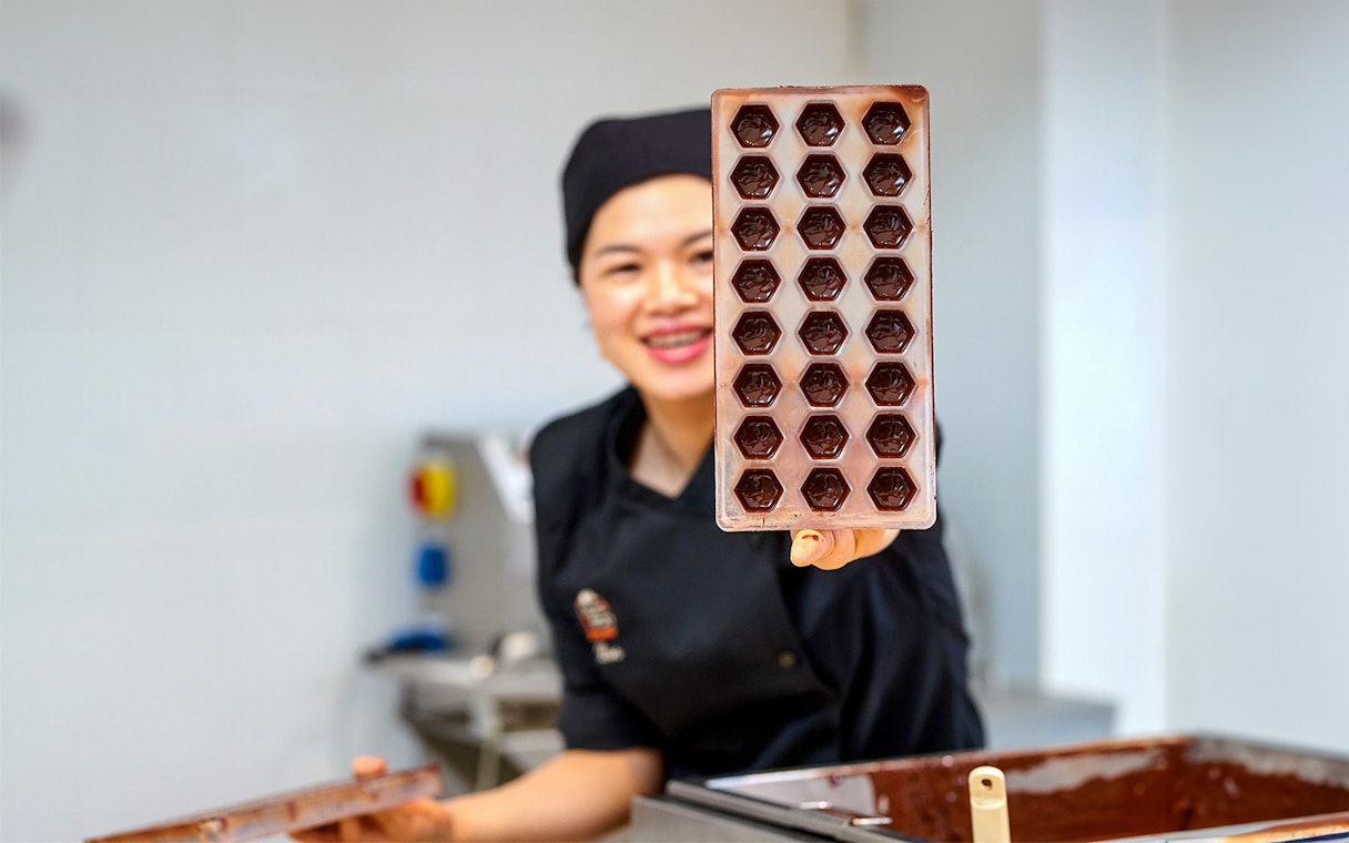 Chocolatier holding a tray of chocolate molds at Choco Story Brussels.