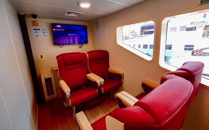 Red seating area inside Sindo Ferry at Tanah Merah Terminal with window view of docked ship.