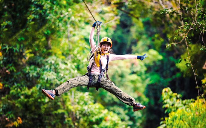 Person ziplining through Daintree Rainforest, surrounded by lush greenery.