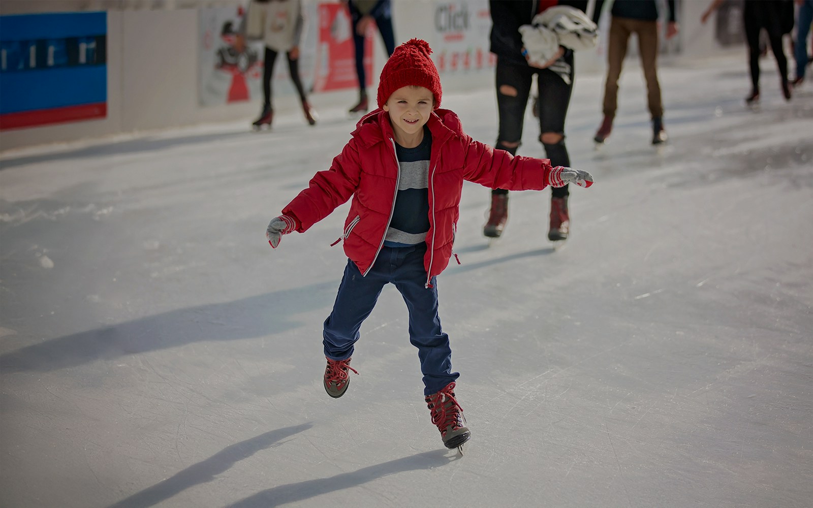 Young boy ice skating on a rink wearing a red jacket and hat.
