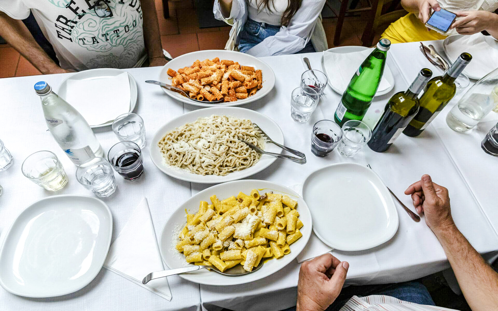 Various pasta dishes with bottles of wine and water on a dining table.