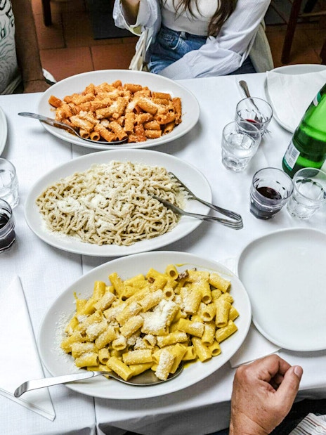 Various pasta dishes with bottles of wine and water on a dining table.