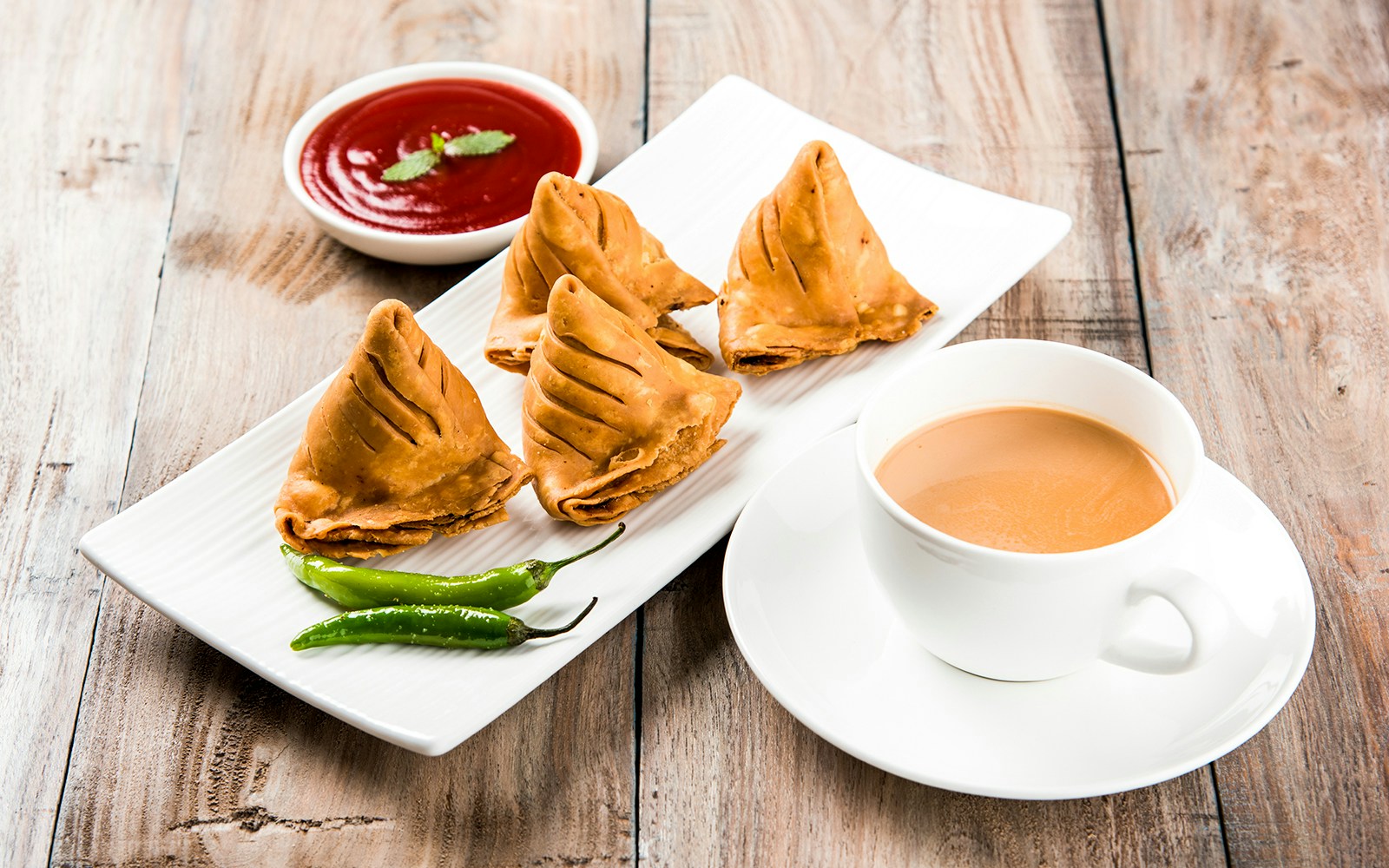 Samosas with tomato ketchup and hot tea on a wooden table.