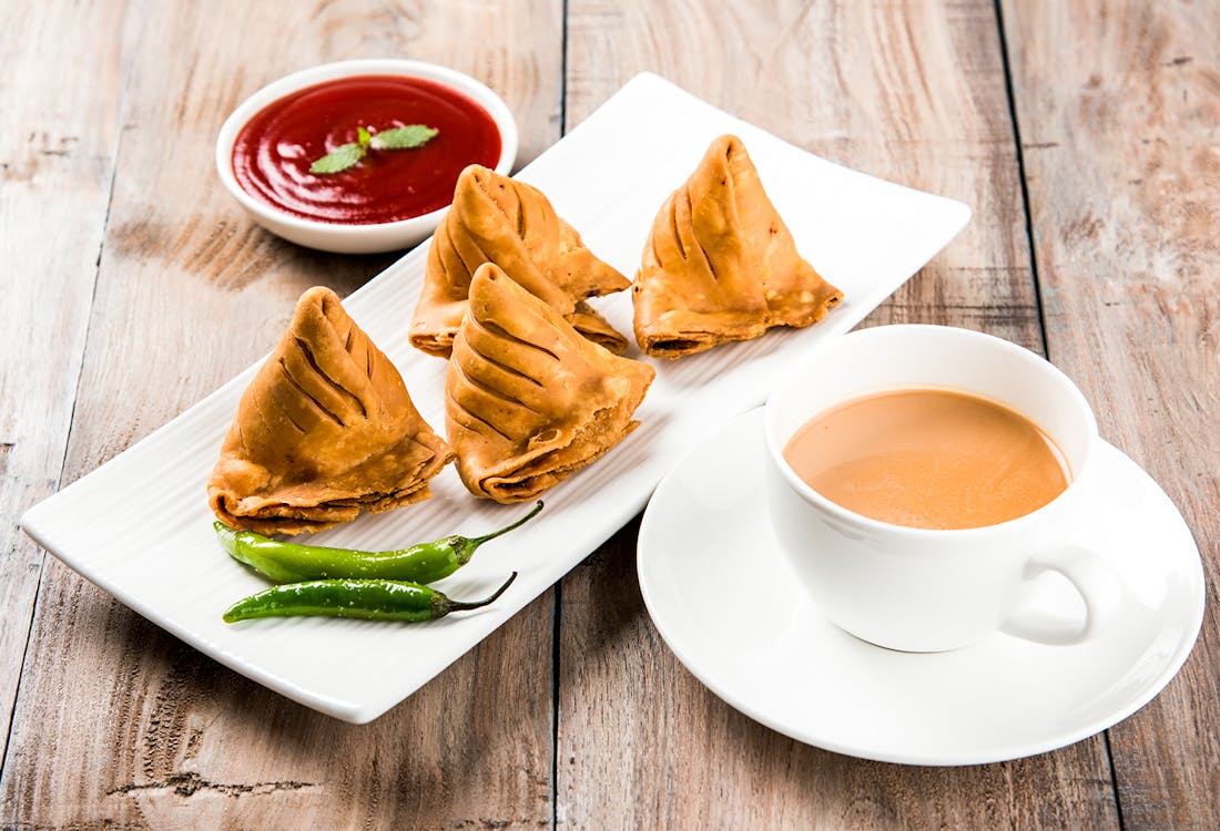 Samosa with tomato ketchup and hot tea on a table.