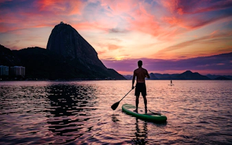 Person paddleboarding at sunrise near Sugarloaf Mountain, Rio de Janeiro.