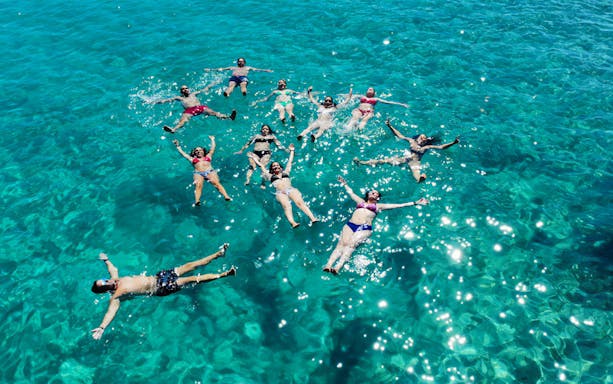 People floating in clear blue water during La Maddalena Archipelago motorboat tour.