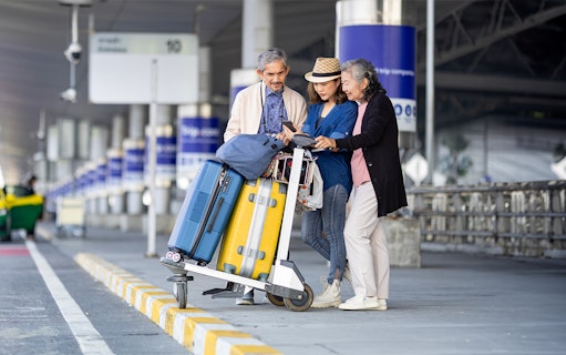 Travelers with luggage at Abu Dhabi Airport, checking phone for Dubai transfer details.