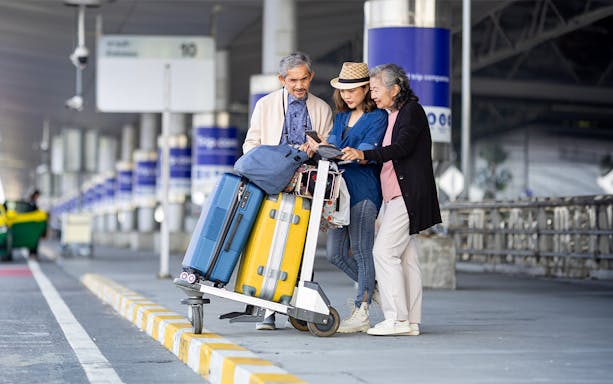 Travelers with luggage at Abu Dhabi Airport, checking phone for Dubai transfer details.